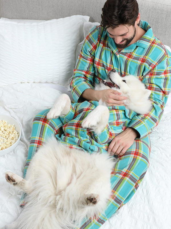 Man in a colorful onesie with two white dogs on a bed.