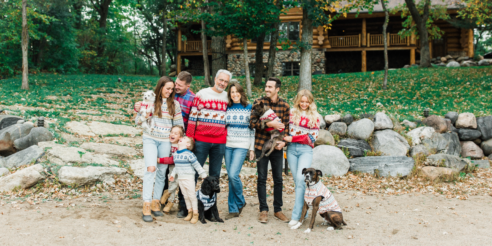 Family with dogs posing in front of a wooden cabin in a forest setting